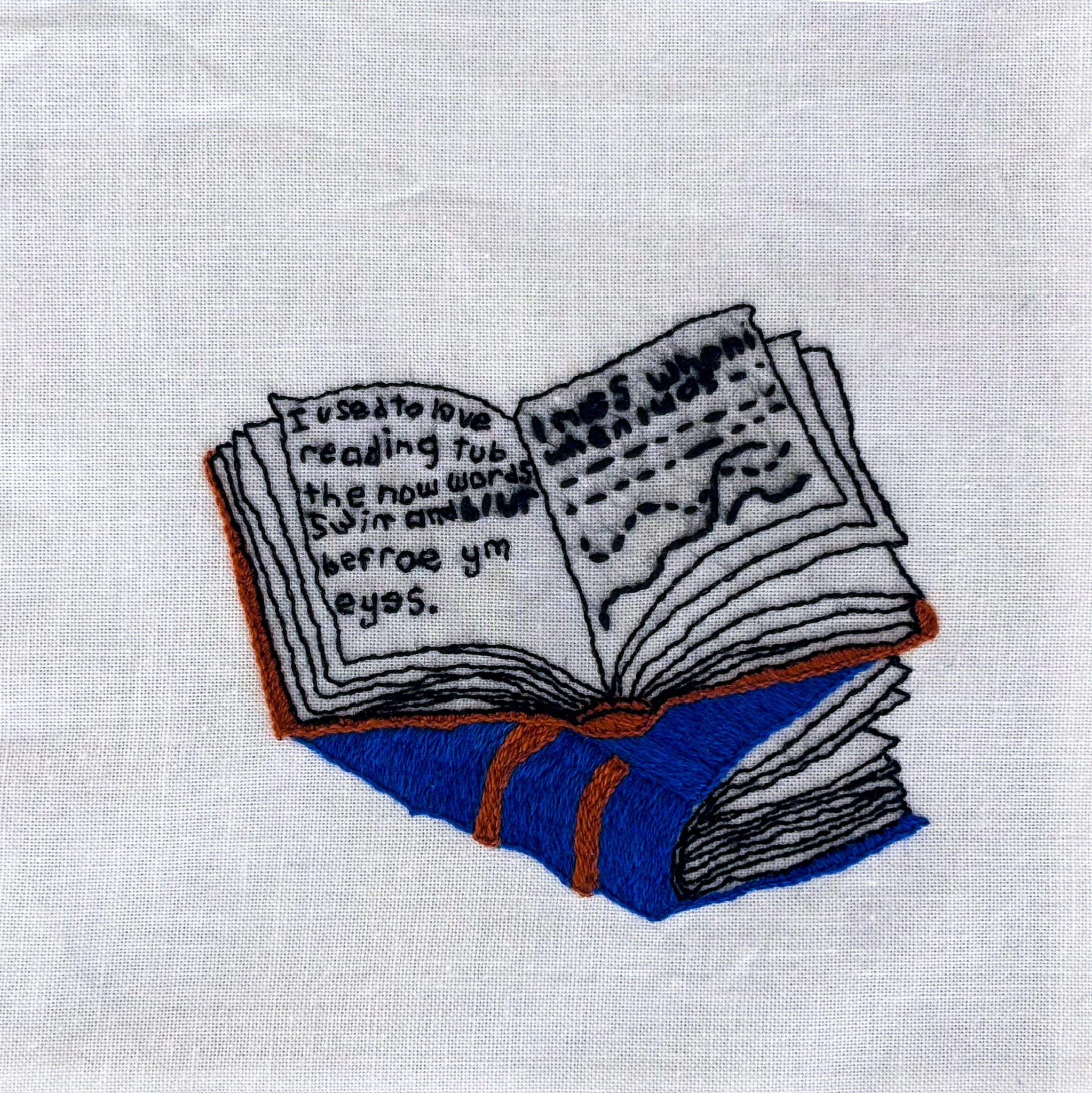 On top of a blue leather-bound book, a brown book lies open, reading “I used to love reading tub the now words swim and blur befroe ym eyes.” in increasingly garbled text. Embroidered on white cotton.