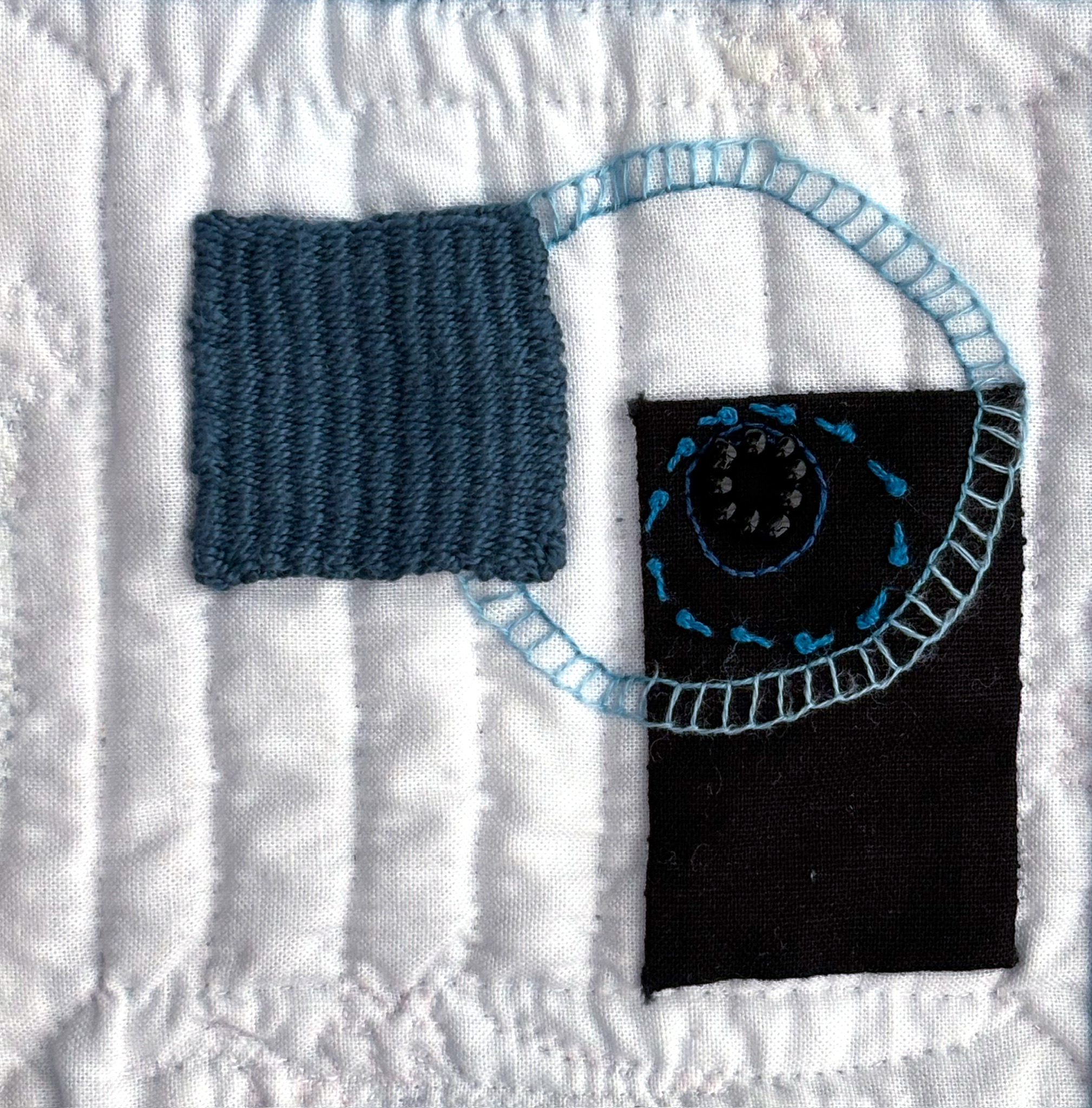 A handwoven blue square and a black cotton rectangle appliquéd on white cotton. Four concentric circles in various shades of blue are embroidered. The innermost circle, made of black beads, sits in the upper left of the black rectangle, down right of the blue weaving while the outermost circle overlaps the rectangle and is partially covered by the blue textile.