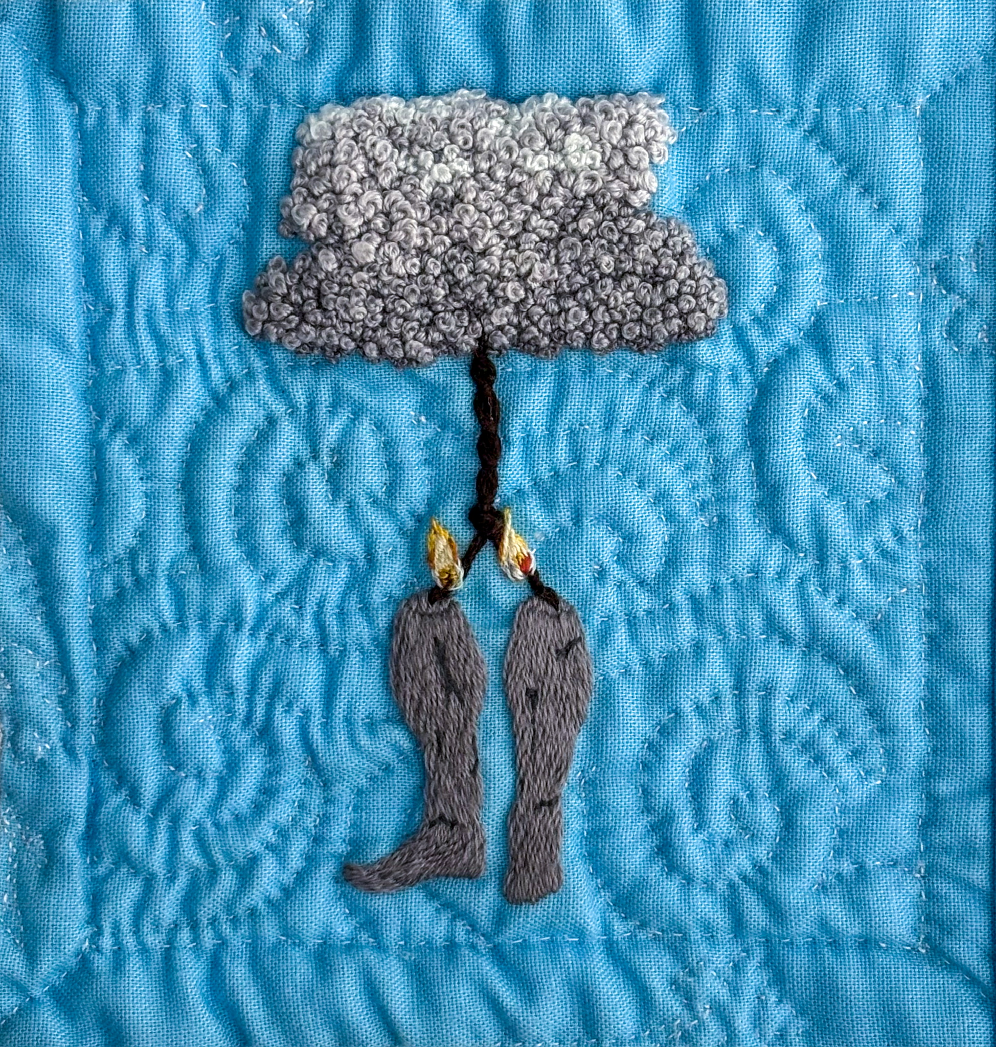 Cracked, concrete lower legs dangle by braided rope from a grey, textured cumulonimbus. Embroidered on blue cotton, twin flames lick up the ropes to the knot where they join.